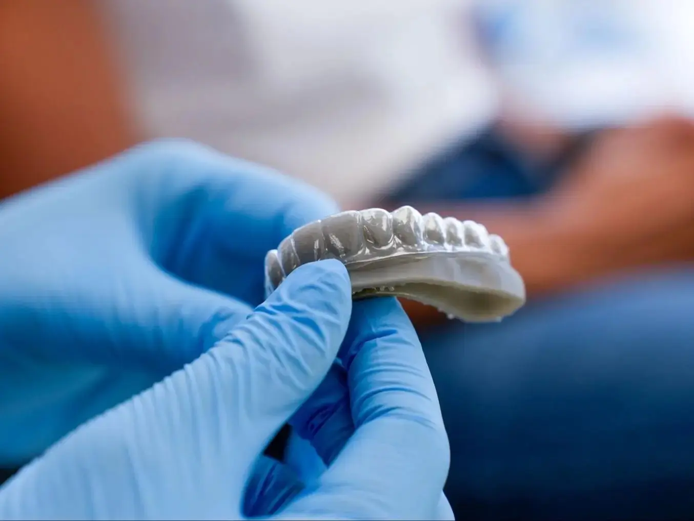 Especialista con guantes sosteniendo un alineador invisible sobre un modelo dental
